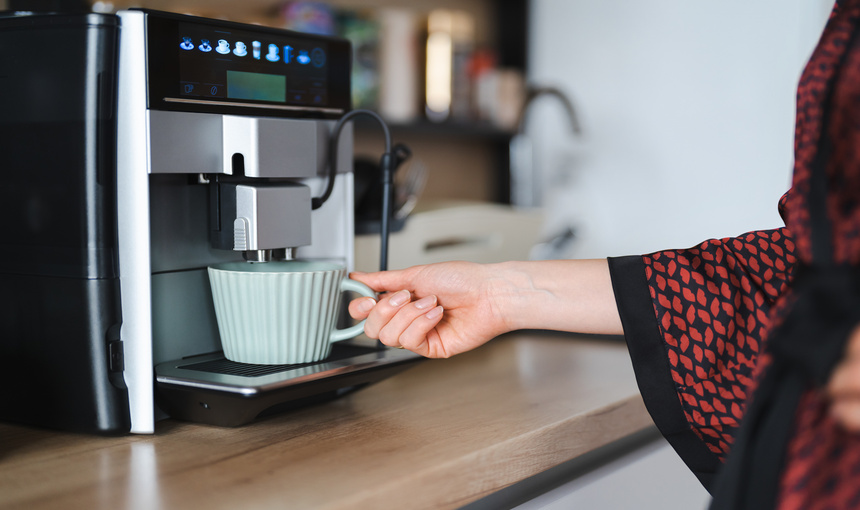 A woman holding a cup at an automatic coffee machine.